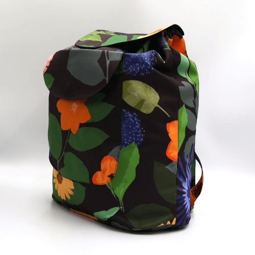 Lightweight backpack with drawstring and bright daisy floral and stripe design on dark brown/black background. Side view.
