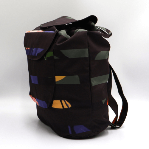 Lightweight backpack with drawstring and bright daisy floral and stripe design on dark brown/black background. Side view.