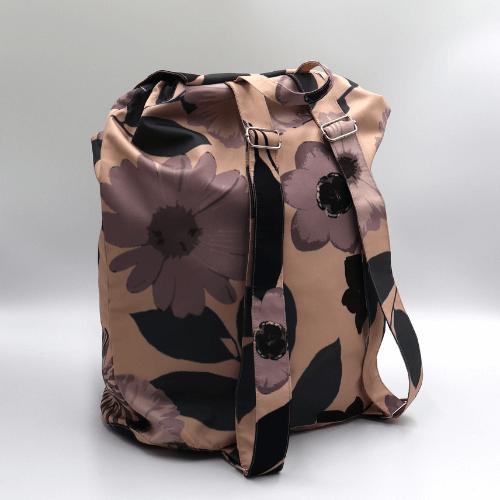Lightweight backpack with drawstring and daisy floral design in mauve and dusky peach. Side angle view.