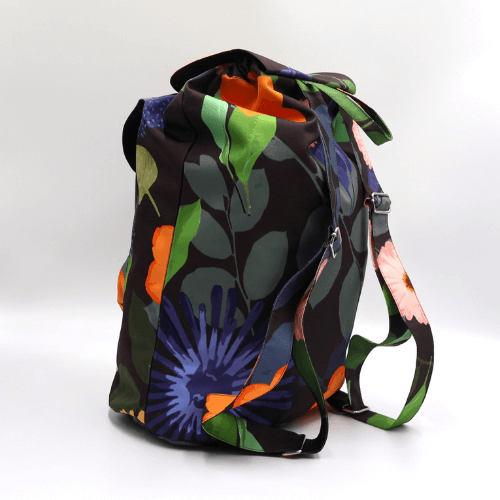 Lightweight backpack with drawstring and bright daisy floral and stripe design on dark brown/black background. Back view.