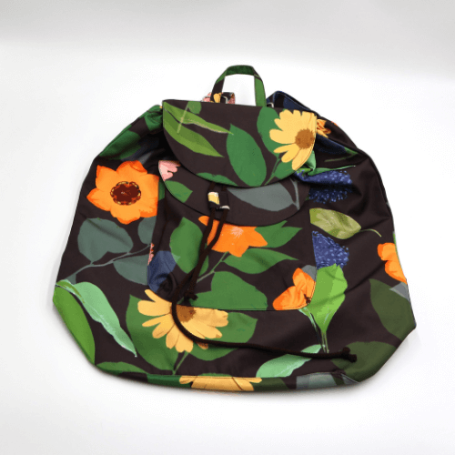 Lightweight backpack with drawstring and bright daisy floral and stripe design on dark brown/black background. Flat view.