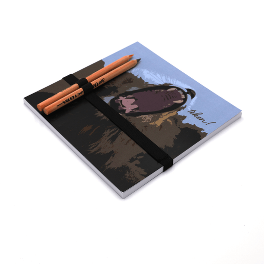 Square art pad with pencils and pencil holder with face of yawning lion on a blue background.