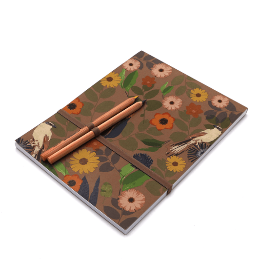 A4 sketchpad with pencils and pencil holder in daisy floral design on brown background.