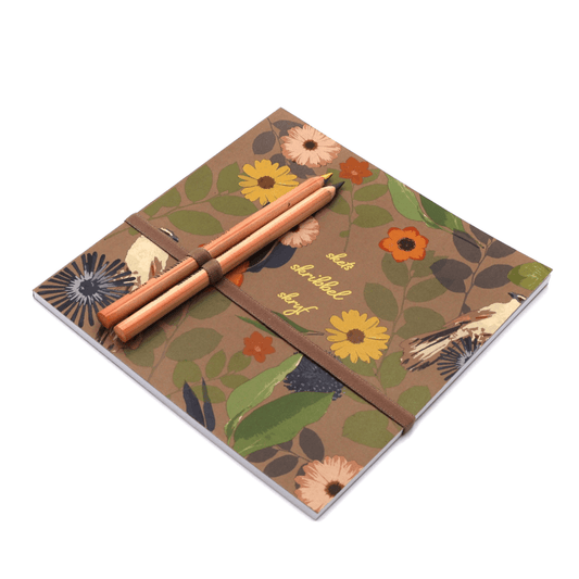 Square art pad with pencils and pencil holder in daisy floral design on brown background. Side binding.