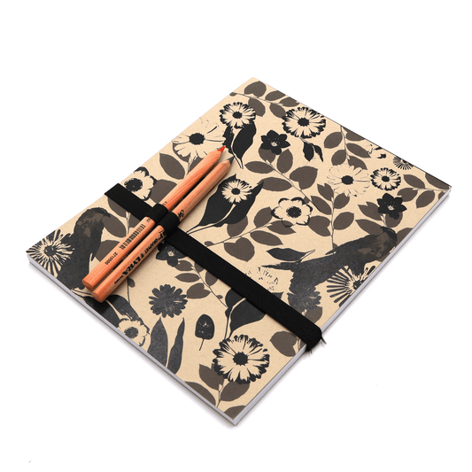 A4 Sketchpad with pencils and pencil holder with daisy floral design in black on a beige sand background.