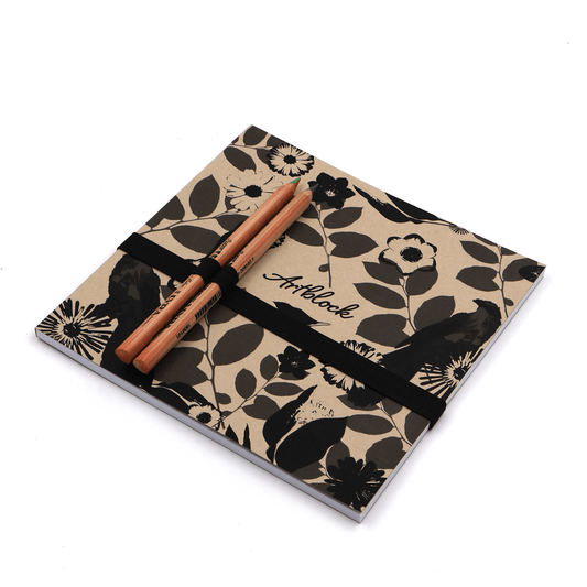 Square art pad with pencils and pencil holder with daisy floral design in black on a beige sand background.