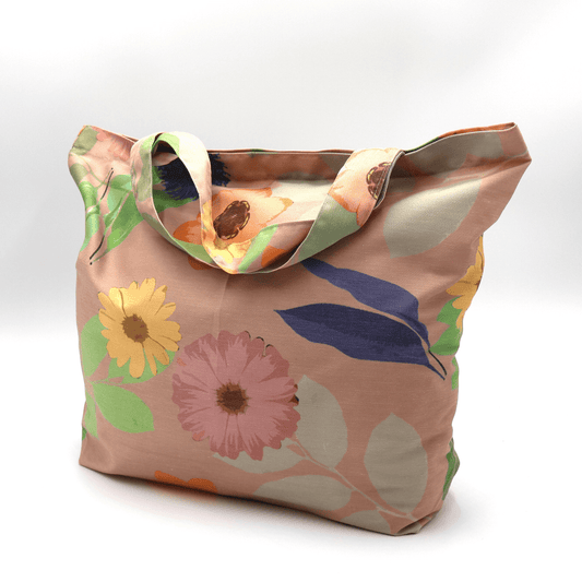 A high-quality tote bag with orange and yellow Daisy floral design on peach background. Side-angle view.