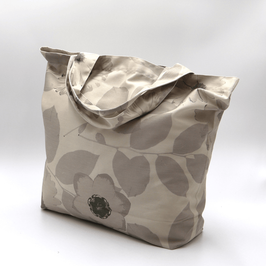 A durable, designer tote bag in light and dark beige daisy floral tones. Side view.