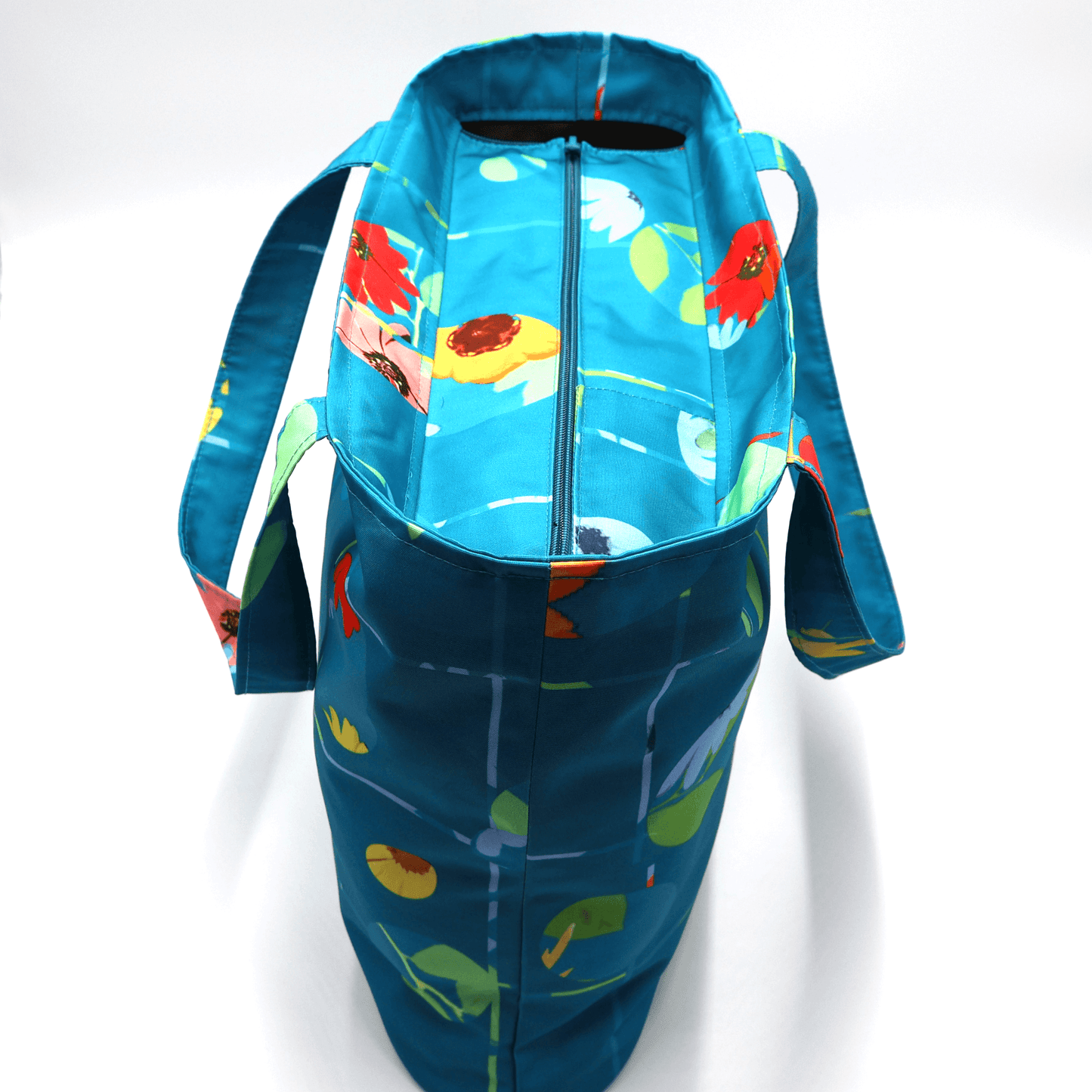 Shoulder bag with bright daisy floral design on blue background. Durable, easy to clean fabric. Top view.