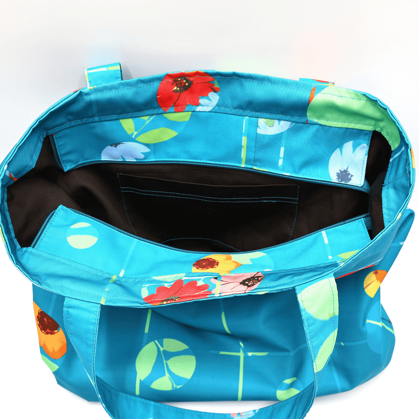 Shoulder bag with bright daisy floral design on blue background. Open top view.