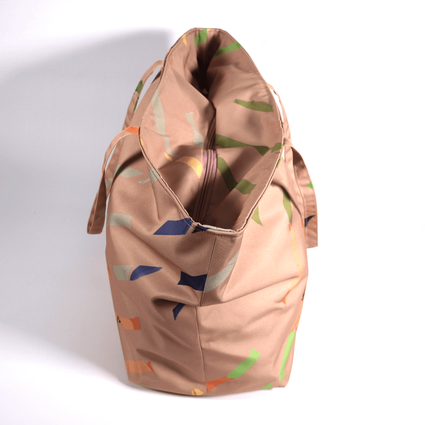 A dusky peach carryall bag with a multi-colour stripe design. Side view.