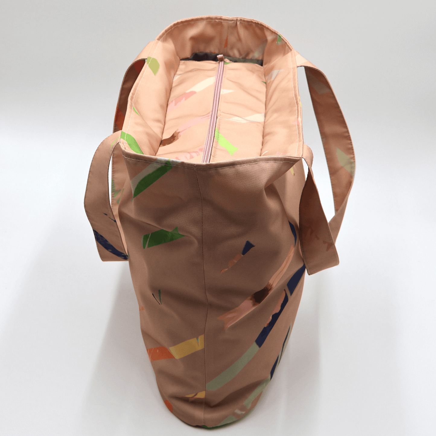 Shoulder bag with bright stripe design on a dusky peach background. Perfect for carrying books and documents. Top view.