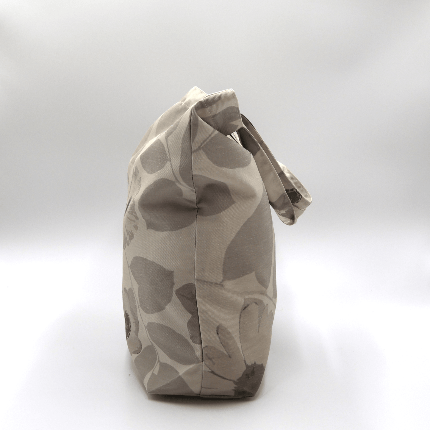 A durable, designer tote bag in light and dark beige daisy floral tones. Side angle view.