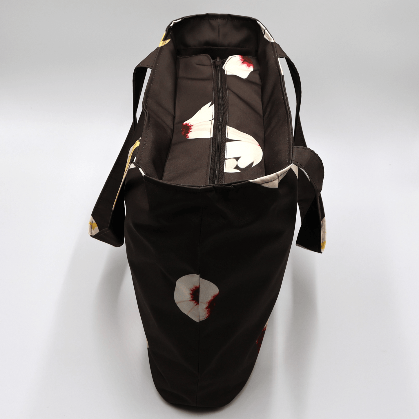 Shoulder bag with white abstract daisy design on a black background. Perfect for carrying books and documents. Top view.
