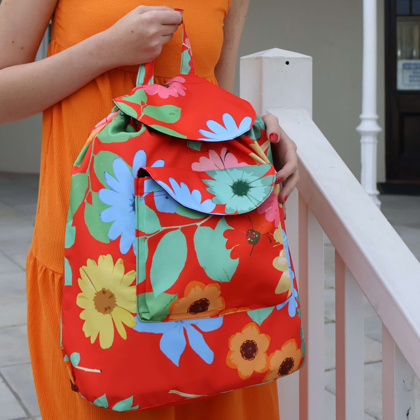 Model holding bright red floral daisy backpack.
