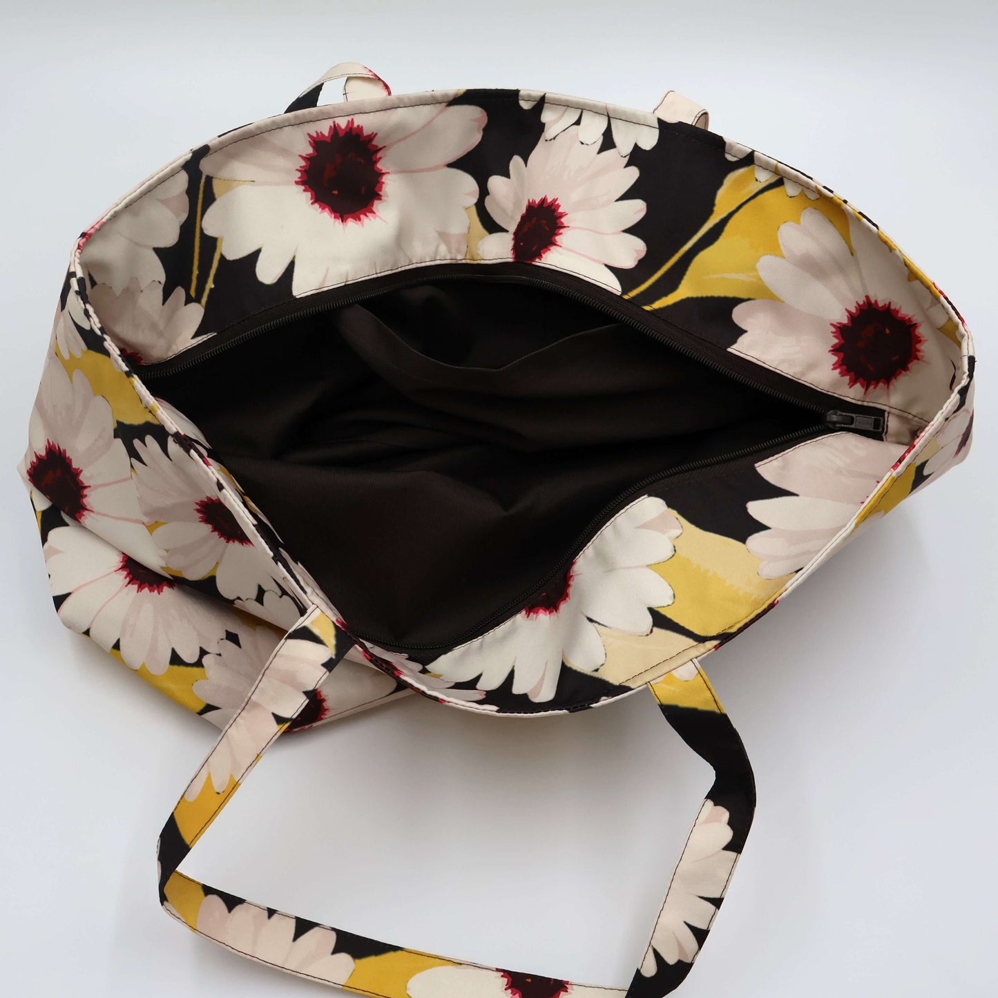 A black carryall bag with big white daisy floral design. Open zipper.