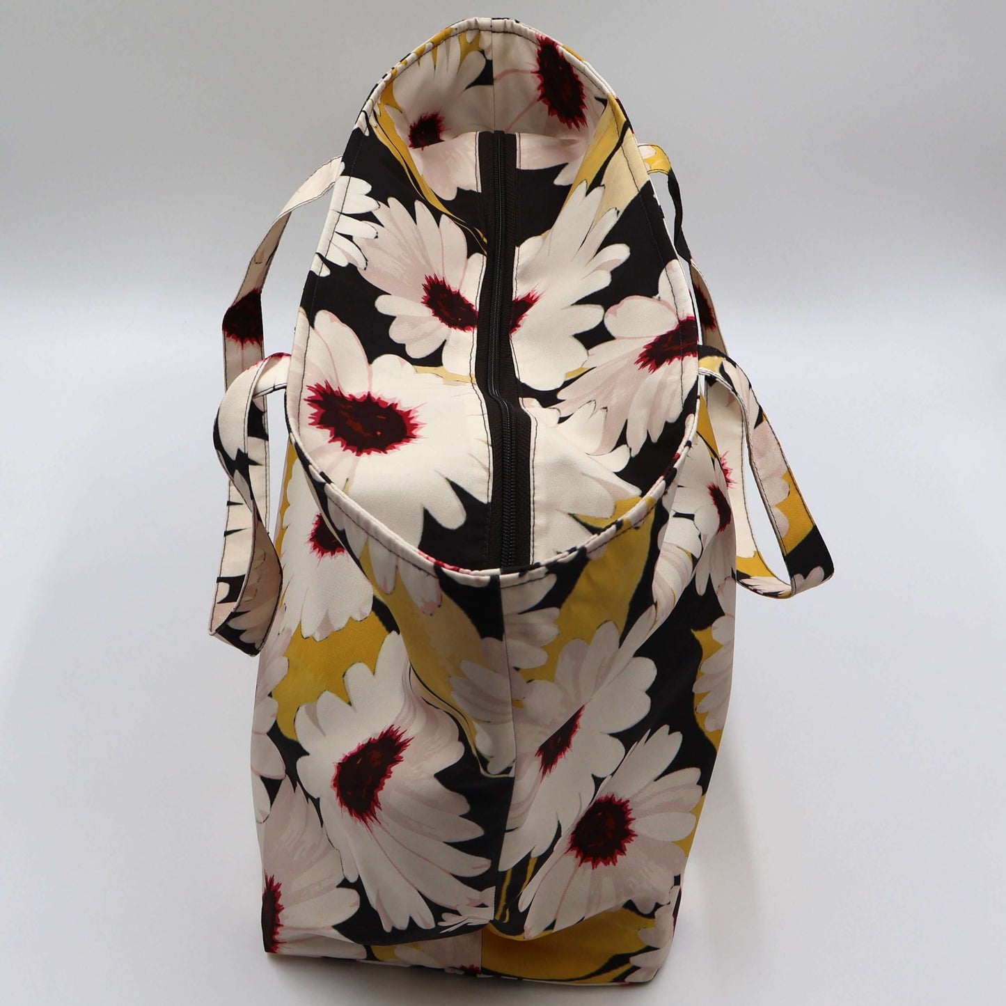 A black carryall bag with big white daisy floral design. Closed zipper.