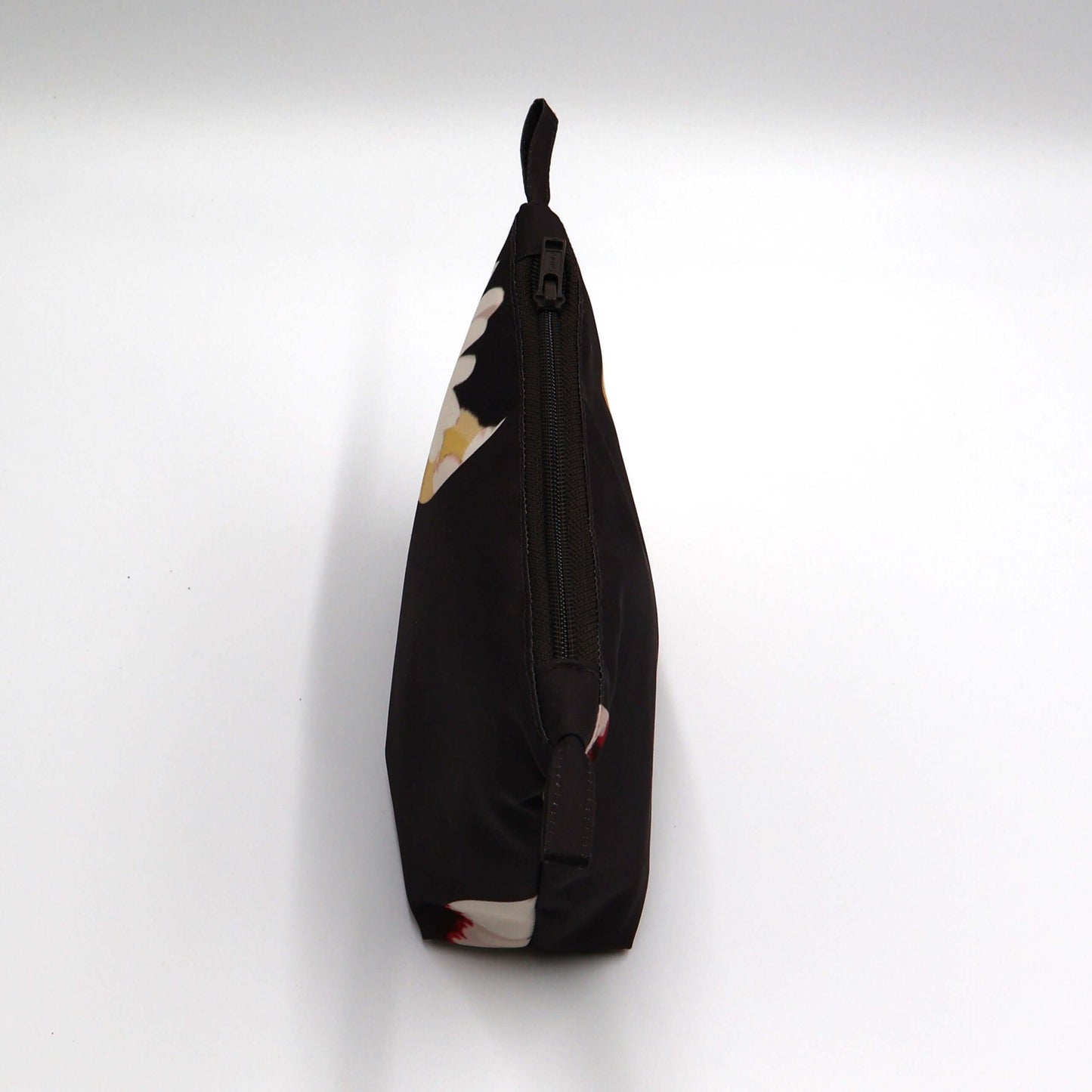 Dark brown/black makeup bag with white daisy floral design, perfect for organizing beauty products. Top view. Closed zipper.