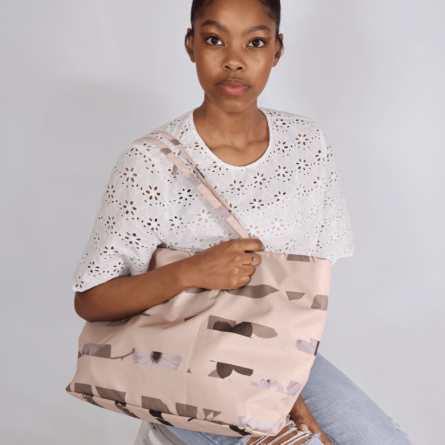 Model with A dusky light peach carryall bag with a stripe design over her shoulder.