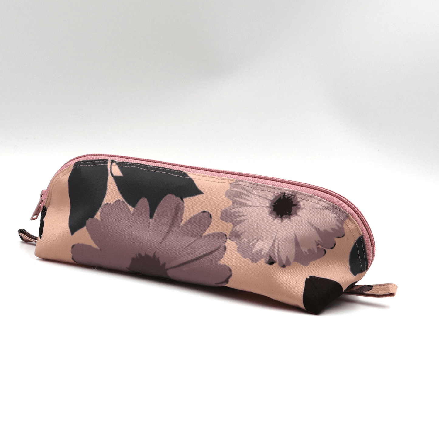 Pencil bag in dusky pink and dark grey daisy floral design on soft peach background. Side view.