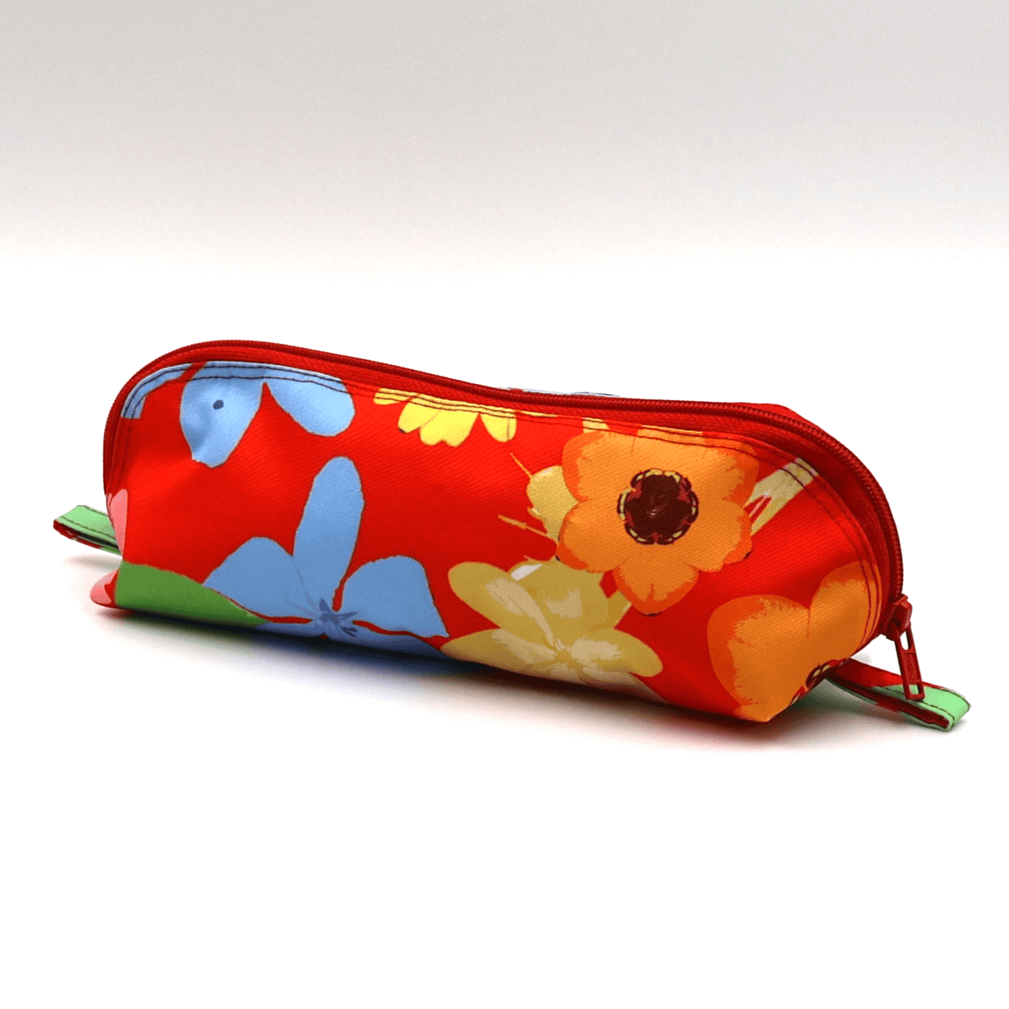 Pencil bag in bright colourful daisy floral design on red background. Side view.