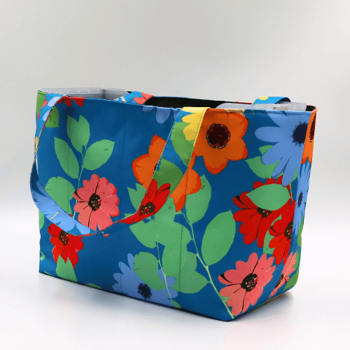 Teacher/book bag with bright floral daisy design on a blue background. Carry books and crafts. Side angle.