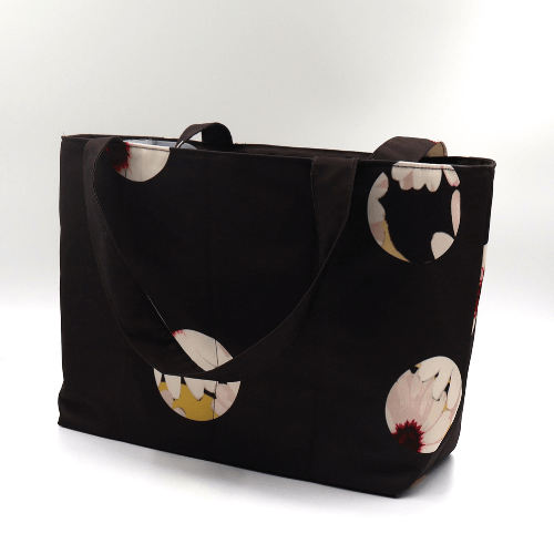 Medium teacher/book bag with white abstract daisy design on a black background. Carry books and crafts. Side view.