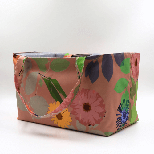 Large teacher/book bag with bright floral daisy design on a dark peach background. Side view.