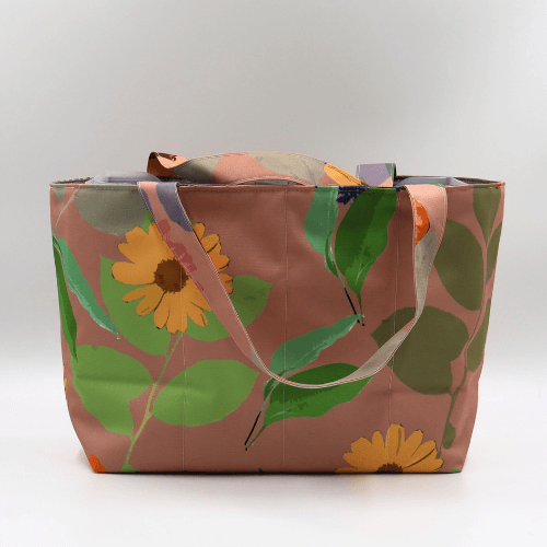 Medium teacher/book bag with bright floral daisy design on a dark peach background.