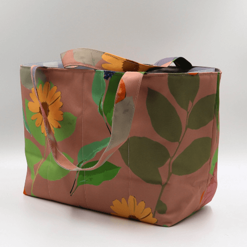 Medium teacher/book bag with bright floral daisy design on a dark peach background. Side angle.