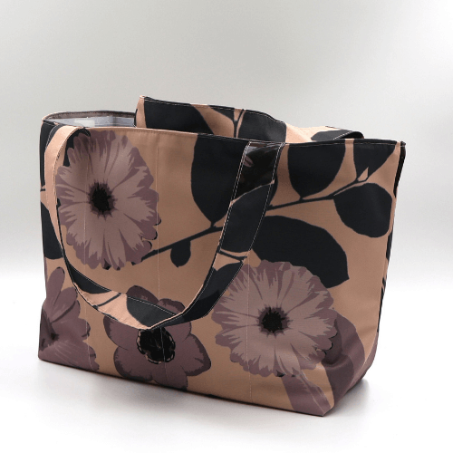 Medium teacher/book bag with daisy floral design in dark and light mauve on a dusky peach background. Side view.