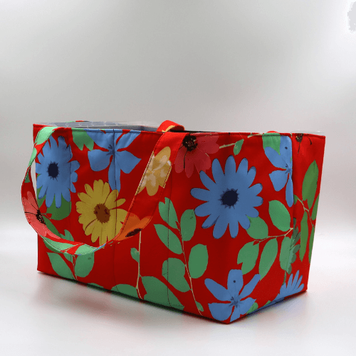 Large teacher/book bag with bright daisy floral design on a red background. Carry books and crafts. Side view.