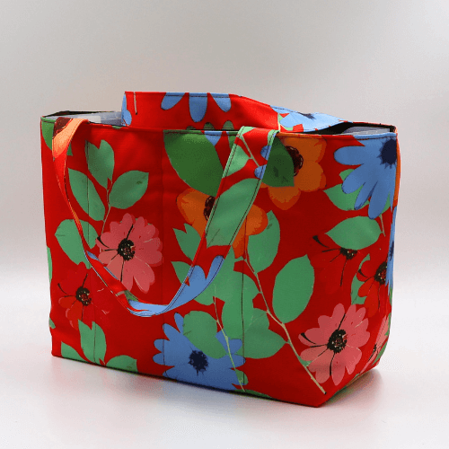 Medium teacher/book bag with bright daisy floral design on a red background. Carry books and crafts. Side view.