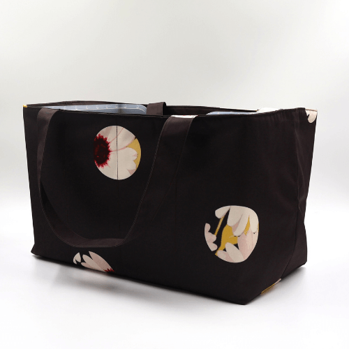 Large teacher/book bag with white abstract daisy design on a black background. Carry books and crafts. Side view.