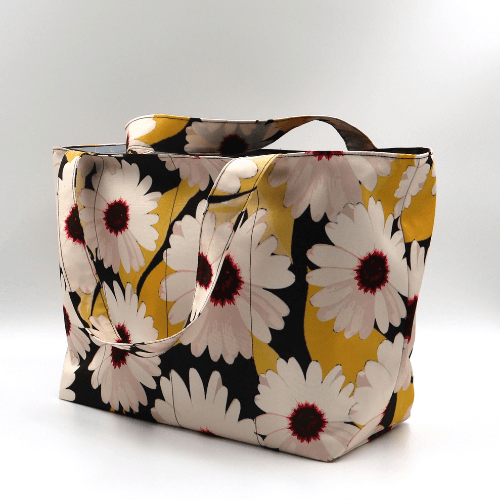 Medium teacher/book bag with white, daisy design on a black background. Side view.