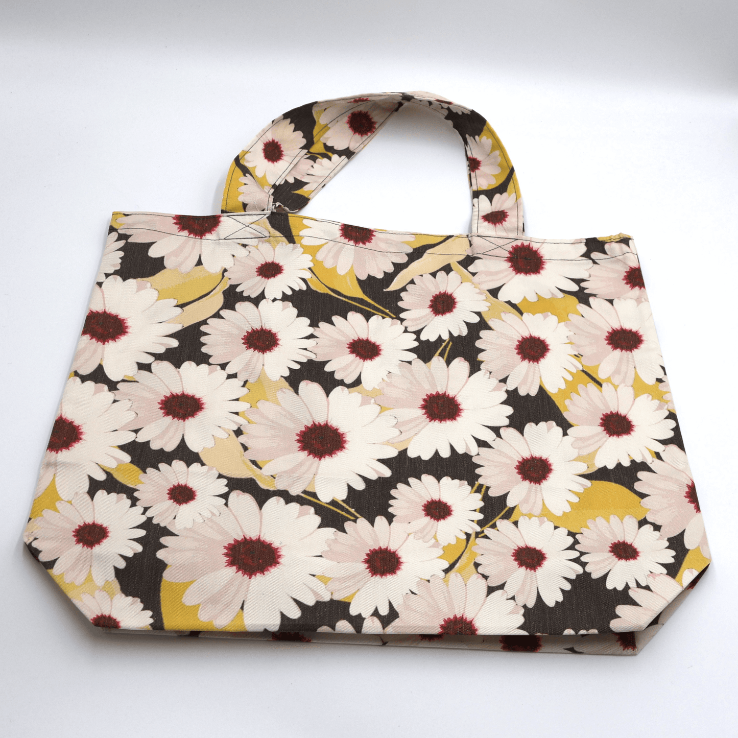 A big, durable tote bag with a white Daisy design. Carry all your daily essentials, books or shopping. Flat view.