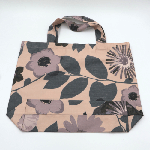 A big, durable tote bag with a mauve and grey daisy design on soft peach background. High-quality materials. Flat view.