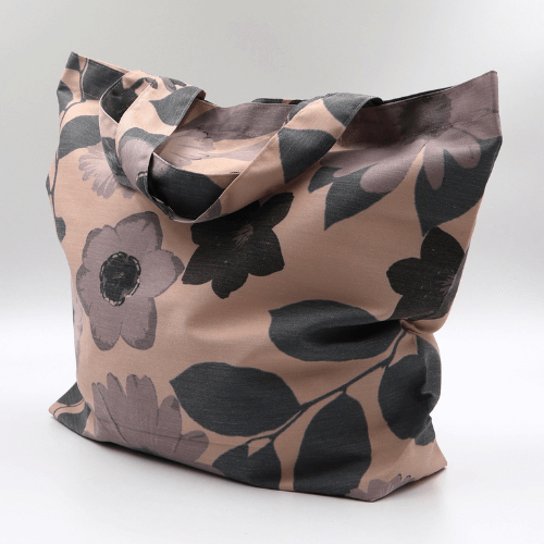 A big, durable tote bag with a mauve and grey daisy design on soft peach background. High-quality materials. Side angle view.