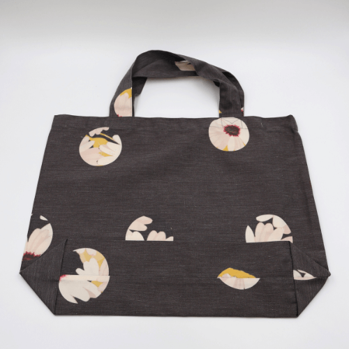 A big, durable tote bag with a white abstract daisy design on black background. High-quality materials. Flat view