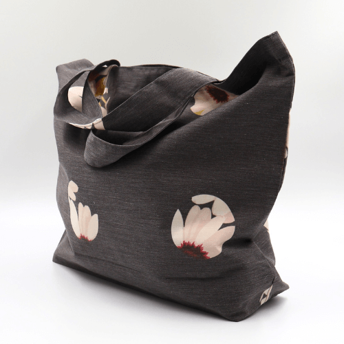 A big, durable tote bag with a white abstract daisy design on black background. High-quality materials. Side angle.
