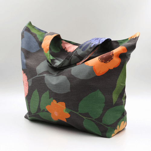 Side view of a big, durable tote bag with a bright orange and yellow daisy design on dark grey background.
