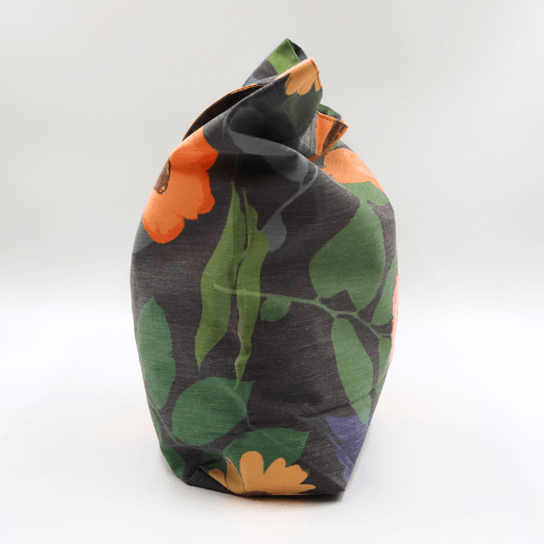 Side view of a big, durable tote bag with a bright orange and yellow daisy design on dark grey background.