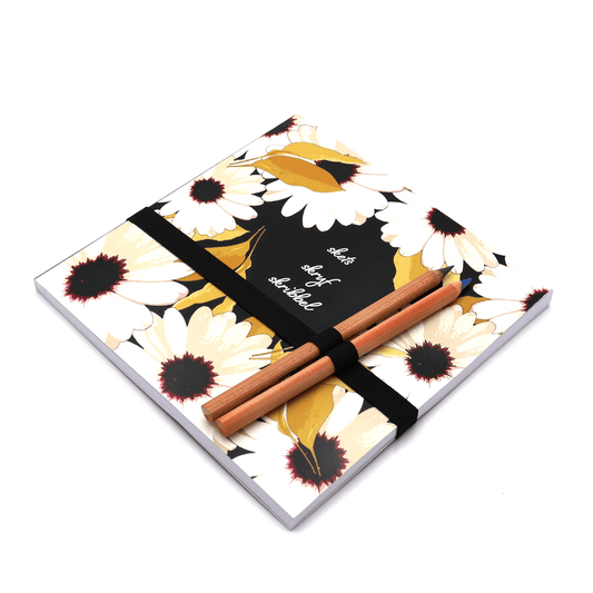 Square art pad with pencils and pencil holder with white daisy floral design on a black background. Side binding.