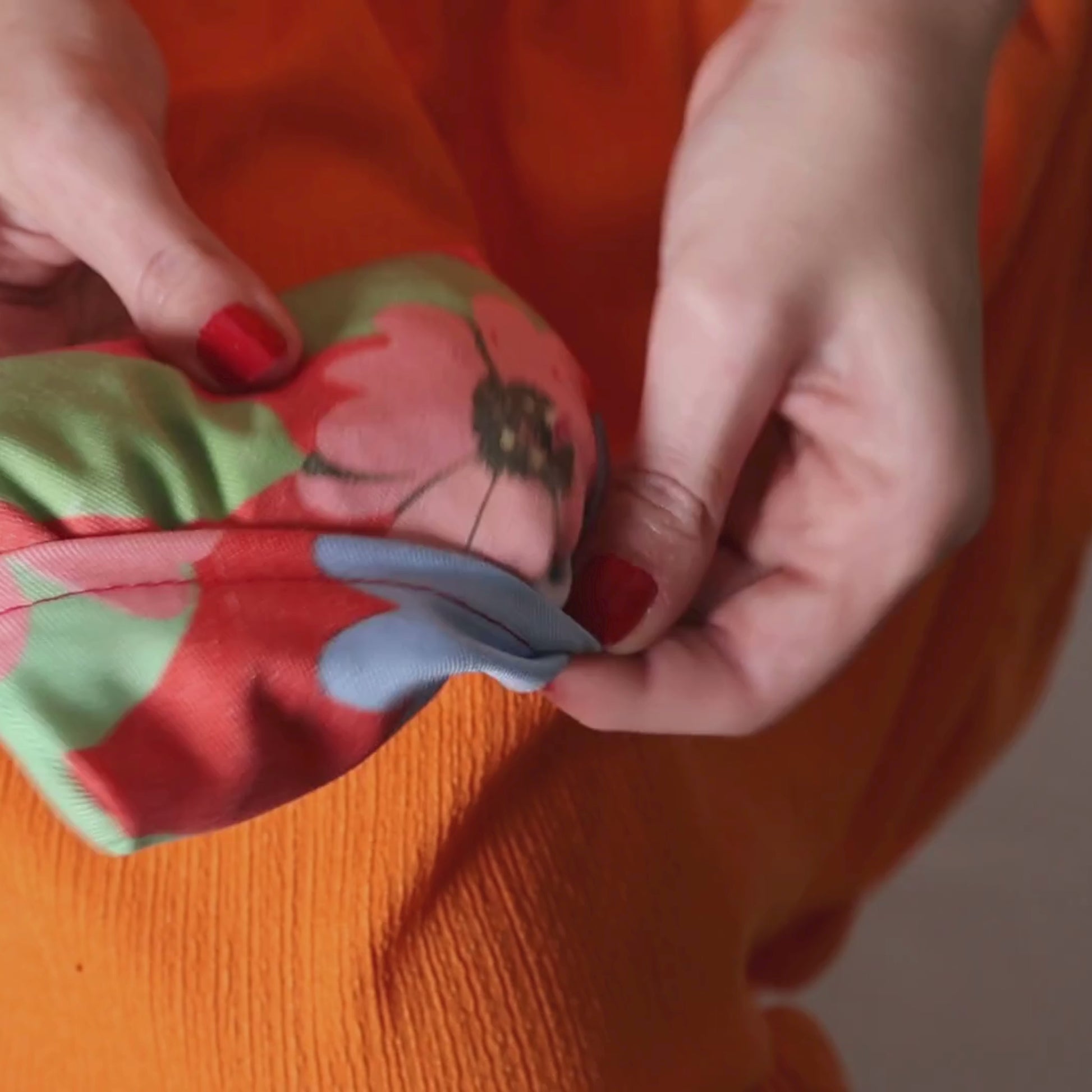 video of fold up shopping bag in bright daisy floral design on peach background.