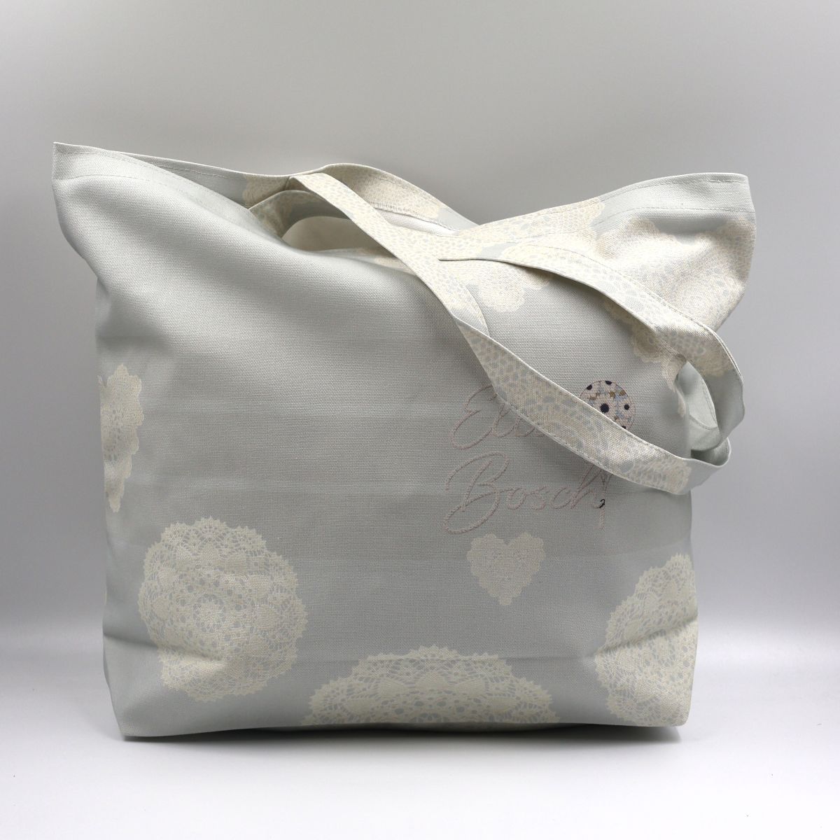 Handmade South African beige cotton canvas tote bag showing the front panel printed with white lace circle and heart motifs on a plain background
