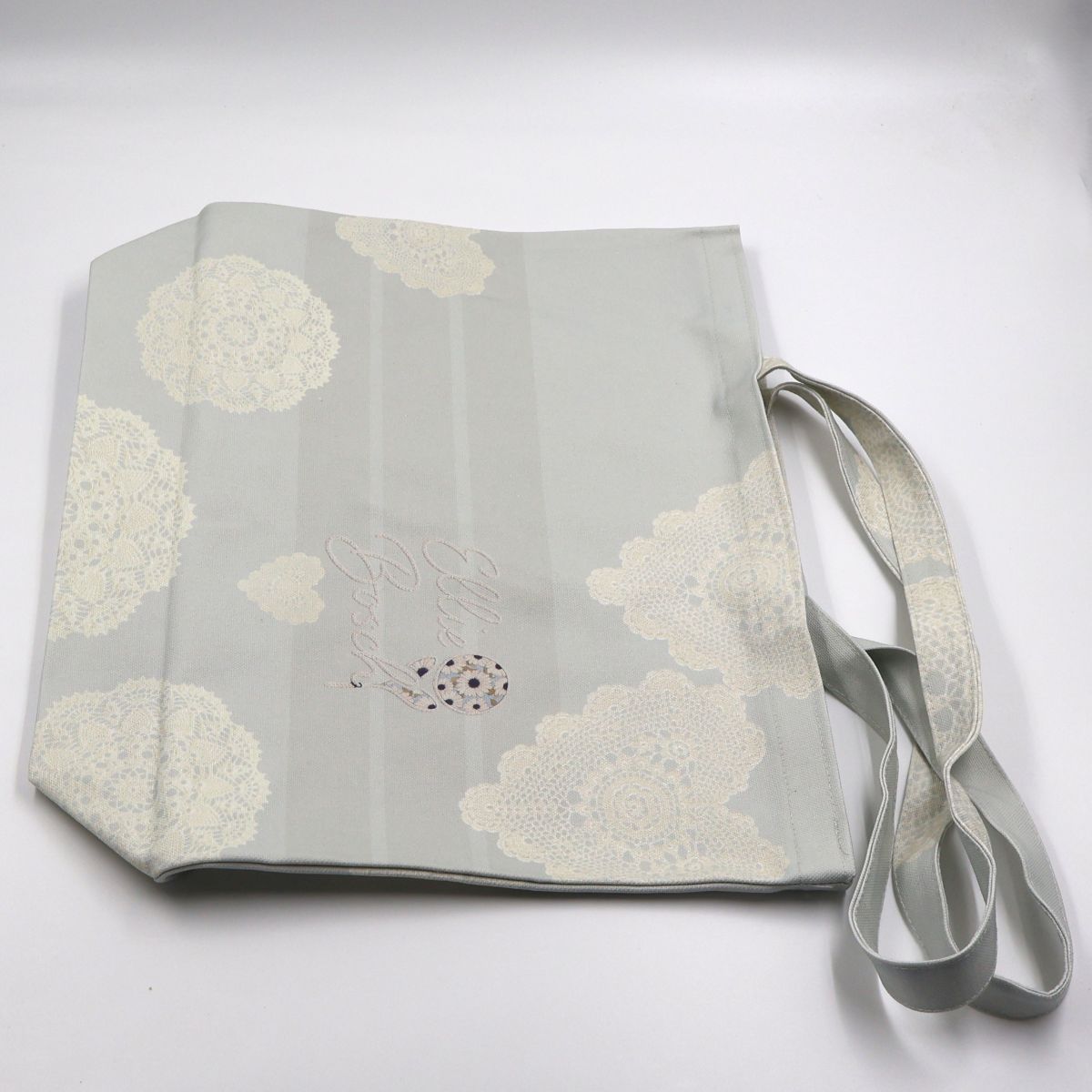 Flat lay view of a wide forty six centimeter by forty two centimeter beige cotton canvas shopper tote displaying the full decorative lace pattern layout