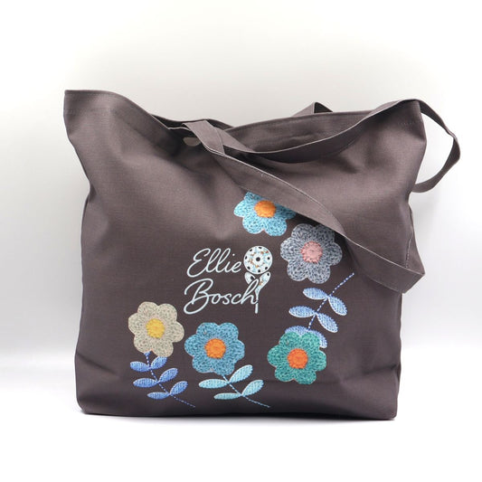A dark brown canvas tote bag with embroidered multicolor flowers and the text 'Ellie Bosch' on the front, set against a plain white background.