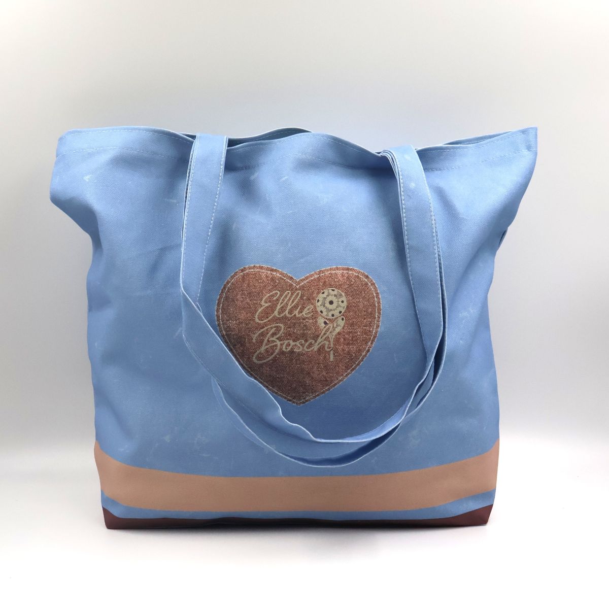 Handmade South African light denim blue cotton canvas tote bag showing the front panel printed with a brown heart motif at the center
