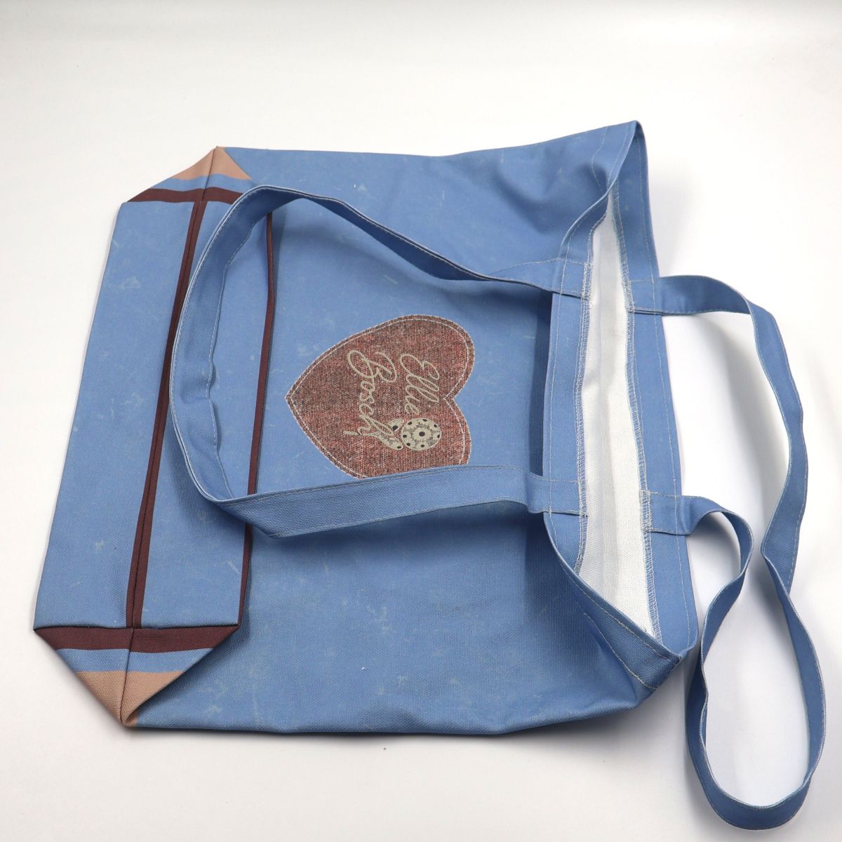 Close up view of a flat laid blue cotton canvas tote bag displaying the high quality neat stitching details along the handle seams