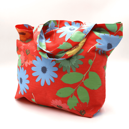 A bright, beautiful tote bag with Daisy design on a red background. Perfect finishes. Side angle view.